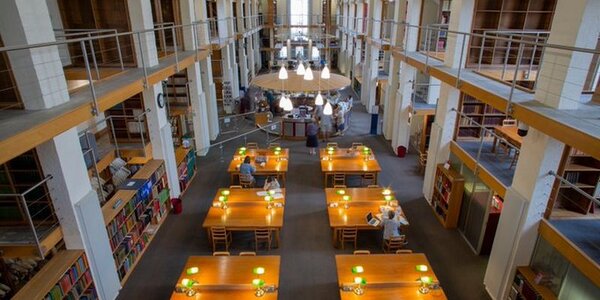 A view looking down on the Library's Reading Room with wooden desks in the centre and different levels of shelving to either side