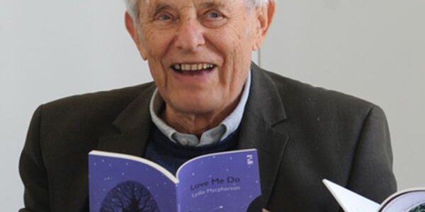 A photograph of the Welsh poet Dannie Abse smiling and holding a book open